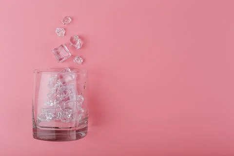 Flat lay with empty transparent glass with spilled ice cubes on pink background Stock Photos