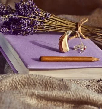 Flat lay features modern hearing aid, lavender bouquet, and a notebook, repre Foto stock