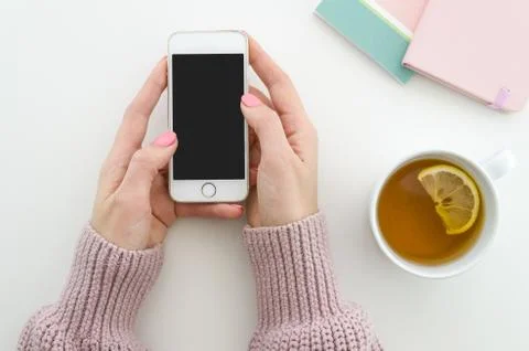 Flat lay. Female hands hold smartphone, cup of tea with lemon and notepads on Stock Photos