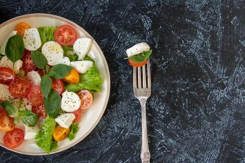 Flat lay with fork and plate of vegetable salad with cheese. serving Caprese Stock Photos