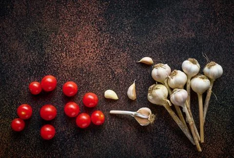 Flat lay of fresh cherry tomatoes with garlic on dark rusty background, top v Stock Photos