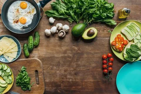 Flat lay with fried eggs in frying pan, pieces of cheese on plate and fresh v Stock Photos