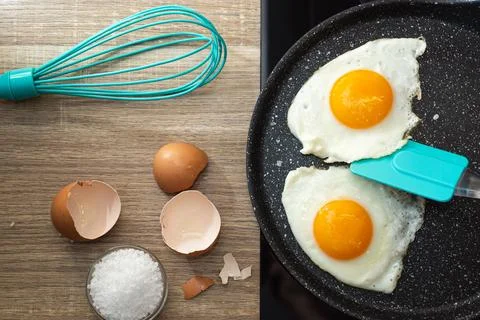 Flat lay of fried eggs with spatula in a frying pan, salt and eggshell on t.. Stock Photos