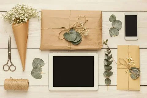 Flat lay of gift boxes, flowers, and tablet on white table Stock Photos