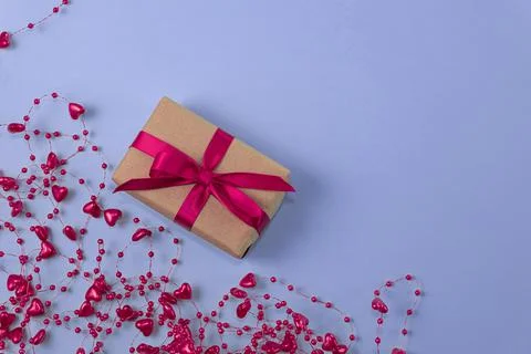 Flat lay of gift with red bow next to beads with hearts on very peri color ba Stock Photos