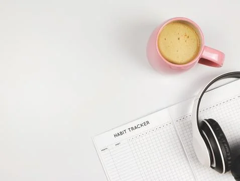 Flat lay of habit tracker book, pink cup of coffee and headphones on white .. Stock Photos
