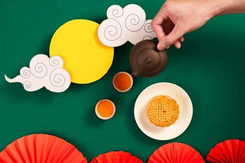 Flat lay of hand holding teapot with mooncake for Mid Autumn Festival Stock Photos