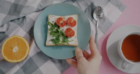 Flat lay of hand putting sandwich on pink table next to orange and cup of tea Stock Footage 236107392