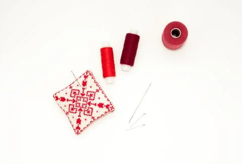 Flat lay with handmade red embroidered needle pad, thread spools, pins, needl Fotos de archivo