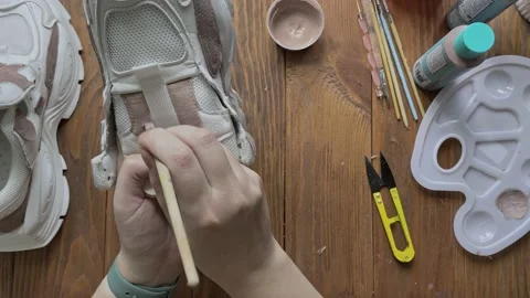 Flat lay of hands paint white boots with brush on wooden table. Stock Footage 165239798