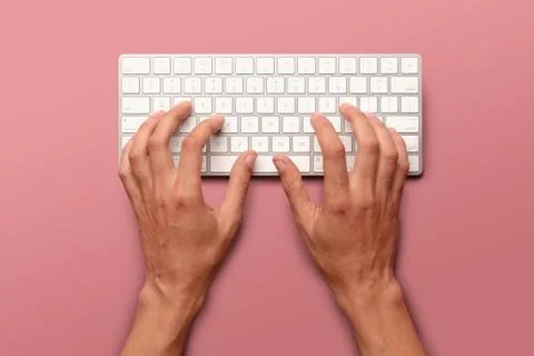 Flat lay with hands typing on white key board on pink table Stock Photos