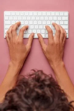 Flat lay with hands typing on white key board on pink table Stock Photos