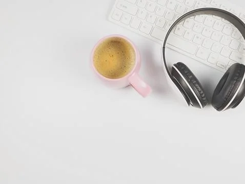 Flat lay of headphones on computer keyboard and pink cup of coffee on white.. Stock Photos