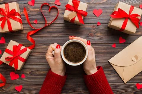 Flat lay of heart shaped cup of black coffee in the hands of women on color.. Stock Photos
