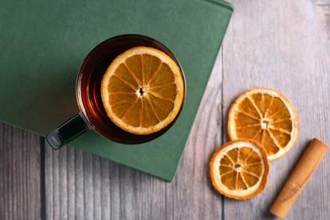Flat lay of hot spiced tea in glass cup with orange slice on green book, rustic Stock Photos