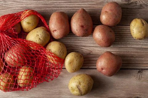 Flat lay image featuring a red mesh potato sack with pink and yellow potatoes Stock Photos