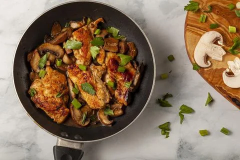 Flat lay image of a non stick frying pan with a chicken breast sautee inside. Stock-Fotos