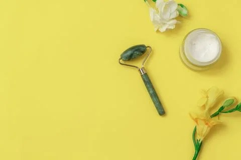 Flat lay with jade roller and flowers on yellow background. Image with copy Stockfoto's
