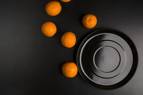 Flat lay of a large black plate and scattered oranges next to it. Foto stock
