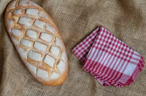 Flat lay loaf of bread and red checkered napkin on burlap. Stock Photos