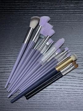 Flat Lay of Makeup Brushes with Purple Handles on Dark Surface Stock Photos