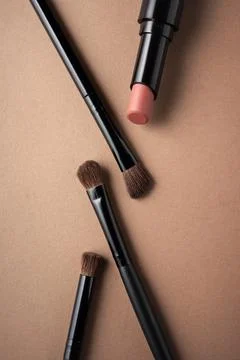 Flat lay of makeup products including lipstick and brushes on neutral backgro Stock Photos