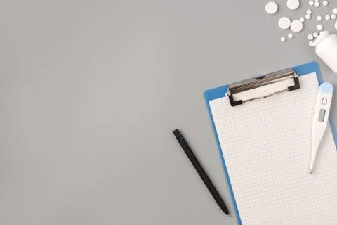 Flat lay of medicine pills, notepad, thermometer on grey background Stock Photos