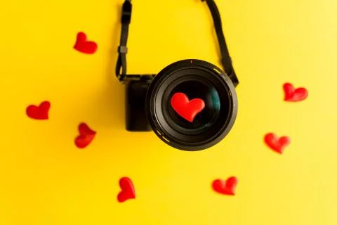 Flat lay of mirorless camera with lens and love red hearts on yellow background Stock Photos