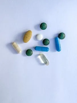 Flat-lay of mixed capsules, tablets, and softgels in various colors on a ligh Stock-Fotos