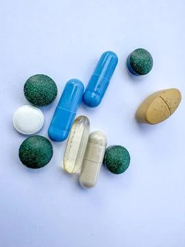 Flat-lay of mixed capsules, tablets, and softgels in various colors on a ligh 스톡 사진