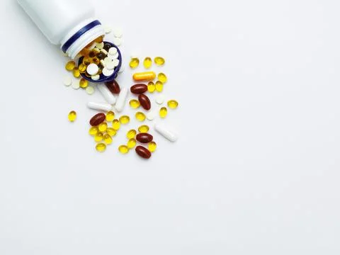 Flat lay with multicolored vitamins and pills, plastic white jar on white Stock Photos