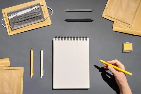 Flat lay notepad, pen, envelope, mask and hand holding pencil on grey background Stock Photos