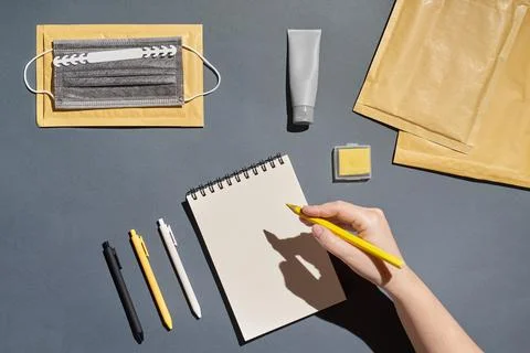 Flat lay notepad, pen, envelope, mask and hand holding pencil on grey background Stock Photos