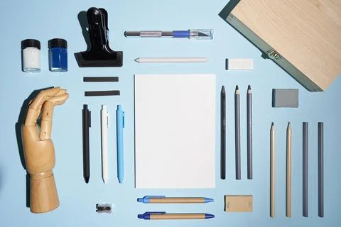 Flat lay notepad, pencils, pens and other drawing staff and wooden hand on blue. Stock Photos