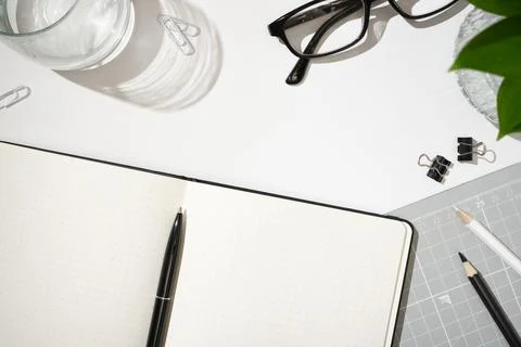 Flat lay of open dotted notebook, black pen, glasses, paper clips, binder c.. Stock Photos