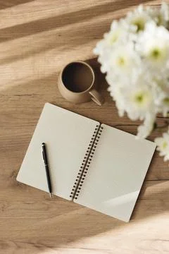 Flat lay of an open notebook, coffee cup, and white chrysanthemum bouquet. Stock Photos