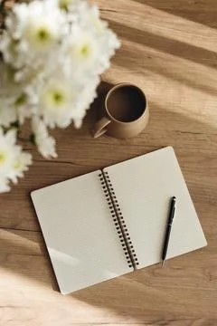 Flat lay of an open notebook, coffee cup, and white chrysanthemum bouquet. Stock Photos