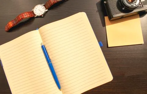 Flat lay of opened notebook, blue pen, mechanical watches, old film camera Stock Photos