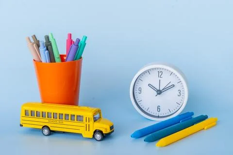 Flat lay with orange cup full of pens clock and toy bus reflecting school s.. Foto stock