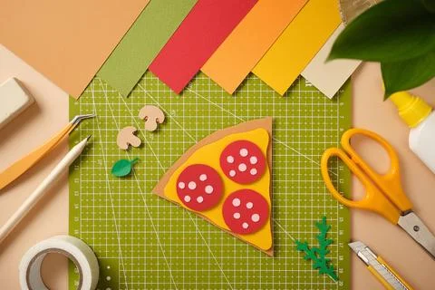 Flat lay of a paper pizza slice with pepperoni on a green cutting mat. Creati Stock Photos