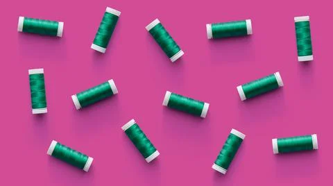 A flat lay pattern of spools of green thread on pink background. Top view Fotos de archivo