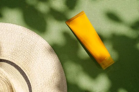 Flat lay rafia hat and orange cosmetic tube on green texture botanical shadows Stock Photos