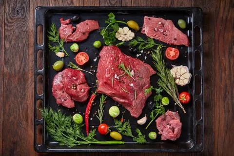 Flat lay of raw beefsteak with vegetables, herbs and spicies on metal tray Stock Photos