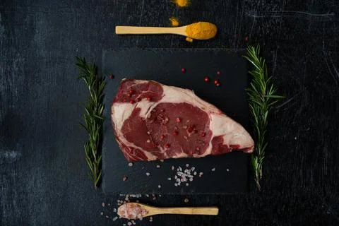Flat lay raw rib eye steak on a square black slate board with two spoons and  Foto stock