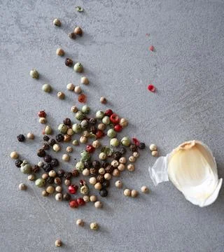 Flat lay with scattered multi-colored peppercorns and peeled garlic clove on rus Stock Photos