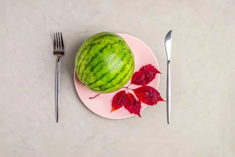 Flat lay serving of small ripe watermelon on pink plate with cutlery. Stock Photos