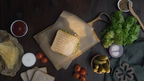 Flat lay shot: man cuts club sandwich in a half by sharp knife on a wooden board Stock Footage 113206788