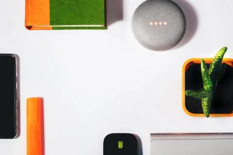 Flat lay of smart speaker with cropped smartphone, green and orange notepad Stock Photos
