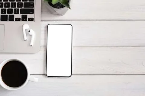 Flat lay of smartphone, coffee, earbuds, and plant on white desk Stock Photos