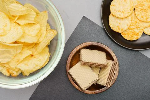 Flat lay of snack, Crispy potato chip and wafer in various bowls over gray ba Stock Photos